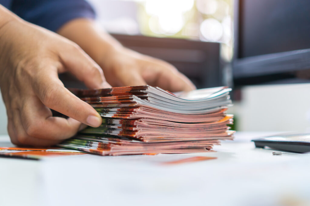 Mains d'une personne organisant une pile de brochures ou magazines colorés sur un bureau, dans un environnement de bureau.
