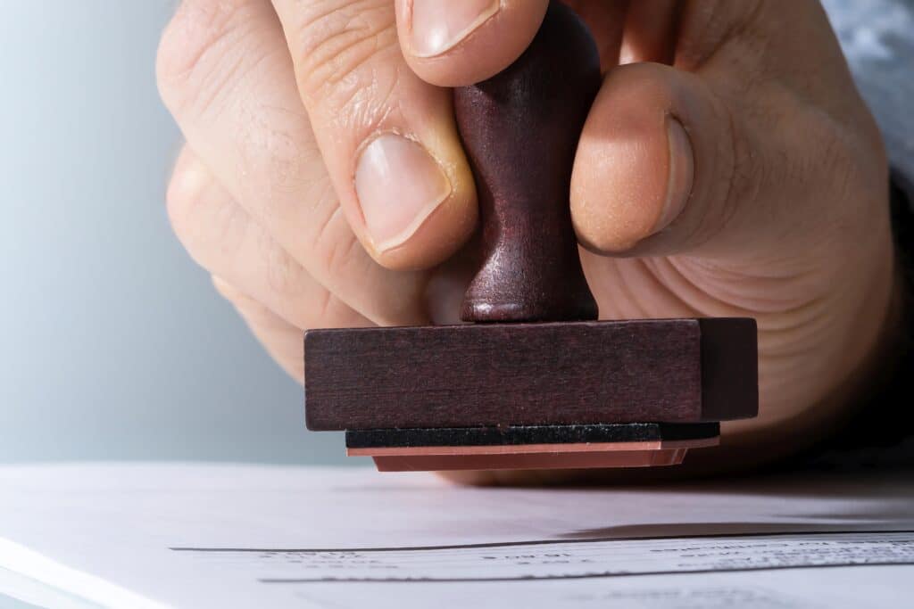 Main tenant un tampon en bois foncé au-dessus d'un document papier, prête à apposer une marque. Vue rapprochée de l'action de signature ou d'approbation.